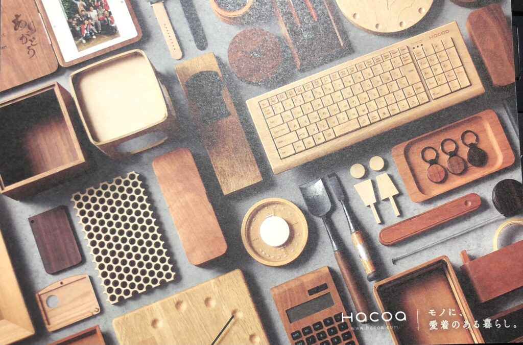 HACOAの商品が掲載されたポストカードの画像。時計、電卓、キーホルダーなど木製商品が陳列されている